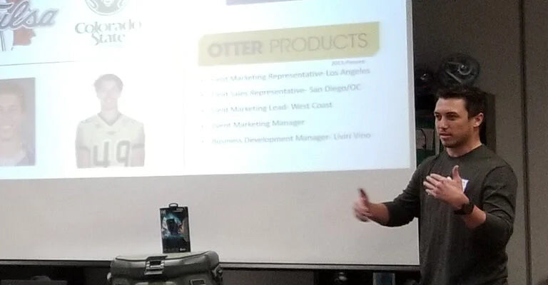 Man giving a presentation in front of a screen displaying 'Other Products' with images and text.