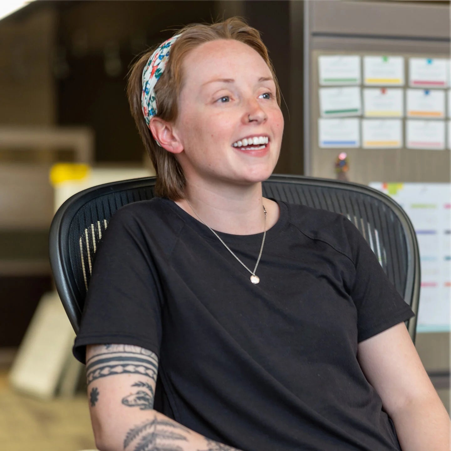 Person sitting in an office chair wearing a black t-shirt with a blurred background